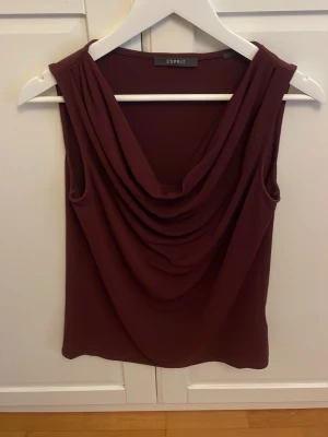 Vinröd draperad topp från Esprit - Snygg vinröd ärmlös topp från Esprit med draperad front och mjukt fall. Perfekt att styla med jeans eller kjol för en trendig look. Materialet känns lent och följsamt mot huden. Den passar till allt och sitter så fint på😻