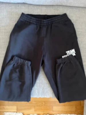 Svarta mjukisbyxor med tryck - Svarta mjukisbyxor med resår i midjan och vid bensluten. Trycket 'TEAM SORTIA' i vitt på ena benet. Perfekta för chill eller träning. Tillverkade i mjukt material för maximal komfort.