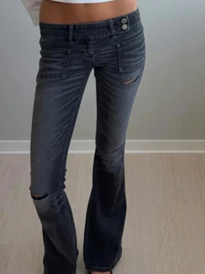 Mörkgrå bootcut jeans  - Snygga mörkgrå bootcut jeans med låg midja och slitna detaljer vid knä och lår. Jensen är bootcut. Dem är ifrån Gina trico 14+ i storlek S .