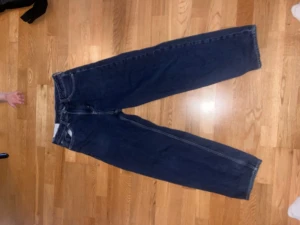 Blå loose fit jeans - Säljer ett par blå loose fit jeans med rak passform och hög midja. Jeansen har klassisk femficksdesign och är tillverkade i denim. Perfekta för en avslappnad och trendig stil.