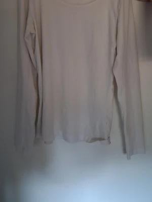 Vit långärmad topp i bomull - En basic vit långärmad topp med rund halsringning. Tillverkad i mjuk bomull som känns skön mot huden. Perfekt att styla lager på lager eller bära som den är. Enkel och clean design utan mönster eller detaljer.