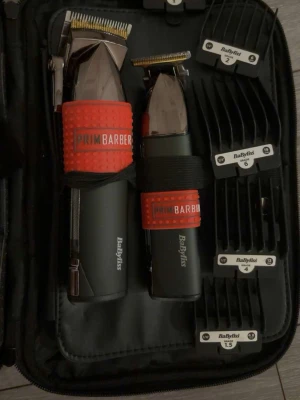 BaByliss klippmaskin set - Snyggt klippmaskin set från BaByliss med två maskiner i svart och silver, båda med röda grepp från PrimBarber. Setet innehåller flera svarta plastkammar i olika storlekar, perfekt för att fixa frisyren hemma. Allt ligger i en praktisk svart väska.