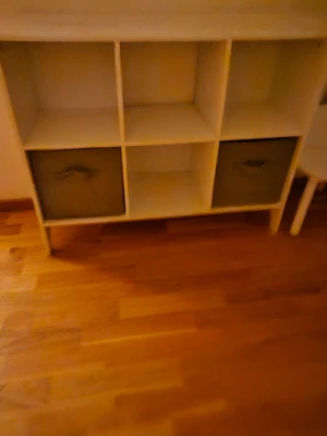 hylla med förvaringslådor barnrum - Säljer en vit hylla med sex öppna fack, varav två innehåller mörkgrå tygförvaringslådor med handtag. Hyllan har en enkel och stilren design och passar perfekt för förvaring av böcker, dekorationer eller annat smått och gott.