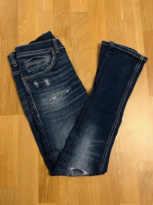 Dondup George  - Säljer ett par mörkblå skinny jeans med slitningar och snygga tvättade detaljer. Jeansen har klassisk femficksmodell och kontrastsömmar. Perfekta för en avslappnad och trendig look. Modellen heter George. Den är sliten vid rumpan(bild 5) men går nog att laga och därför säljer jag den för 200. Förutom hålet är jeans i top skick. Storleken är 29.