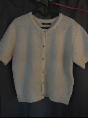 Stickad tröja med knappar  - Supermjuk och fluffig vit kofta från Gina Tricot med korta ärmar och rund hals. Koftan har snygga pärlknappar framtill och är gjord i ett stickat material som känns riktigt cozy. Tyvärr har det blivit ett hål som man ser på andra bilden, det syns inte jätte mycket på och går att sy igen för den som vill det. Annars jätte fin och perfekt till hösten. Helt slutsåld, säljs för att den inte kommer till användning.