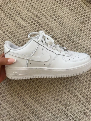 Vita Nike Air Force 1 sneakers - Klassiska vita Nike Air Force 1 sneakers i läder med perforerad tå, vit sula och matchande vita skosnören. 