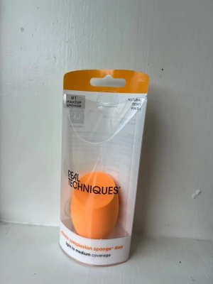 Real Techniques orange beautyblender - Miracle Complexion Sponge från Real Techniques i en klar orange färg. Den har en rundad form med en platt sida för enkel applicering av foundation och andra flytande produkter. Tillverkad i mjukt, latexfritt material för en naturlig finish. Aldrig använt. 
