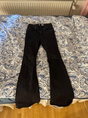 Svarta utsvängda jeans - Säljer ett par svarta jeans med utsvängda ben och klassisk femficksmodell. Jeansen har hög midja och är tillverkade i ett stretchigt material som sitter snyggt. Perfekta för dig som gillar en retro och trendig look.