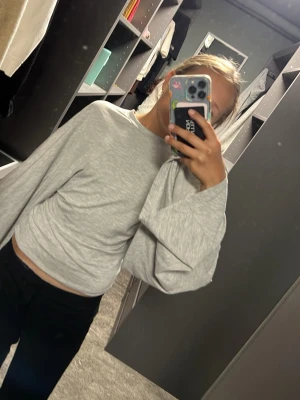 Grå sweatshirt med vida ärmar - Säljer en ljusgrå sweatshirt med oversized, vida ärmar och rund hals. Tröjan har en avslappnad passform och är gjord i mjukt sweatshirtmaterial. Perfekt för dig som gillar en chill och trendig stil.