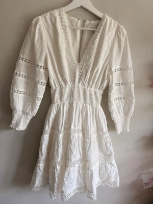 Vit kort BY MALINA klänning med spetsdetaljer - Superfin vit kortklänning med v-ringning, spetsdetaljer och trekvartsärmar. Den är från By malina och har blivit sparsamt använd och är i gott skick! 