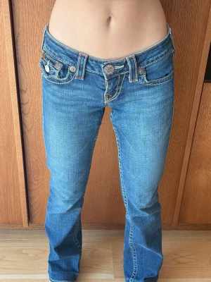 True Religion Jeans ❤️ - Snygga blå low waist jeans med bootcut fit och tydliga kontrastsömmar i storlek W25. Jeansen har dekorativa fickor både fram och bak, samt stora knappar och detaljerade broderier på bakfickorna. Jag säljer dem då de är för stora på mig. Det finns inga defekter!!