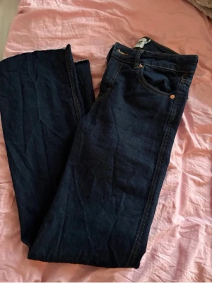Mörkblå bootcut jeans - Snygga mörkblå bootcut jeans med klassisk femficksdesign och orangea sömmar. Jeansen har normal passform och är tillverkade i bomull med en lätt stretchig känsla. Perfekta till en avslappnad och trendig look. De är avklippta längst ner. 