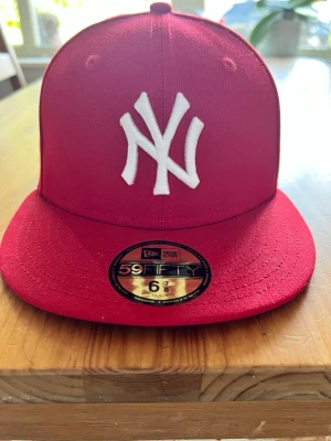Röd New Era 59FIFTY NY keps - Snygg röd New Era 59FIFTY keps med vit New York Yankees-logga framtill. Klassisk flat brim och broderade ventilationshål🤩 Tillverkad i bomull och polyester för en bekväm passform. Perfekt för dig som vill ha en stilren och sportig look😎