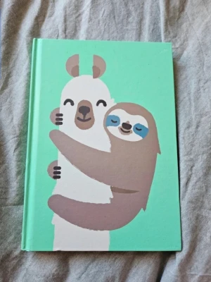 Grön anteckningsbok med djurmotiv - Söt anteckningsbok med hårt grönt omslag och illustration av en sengångare som kramar en lama på framsidan. Baksidan har en glad sengångare med armarna i luften. Perfekt för anteckningar, dagbok eller skisser.