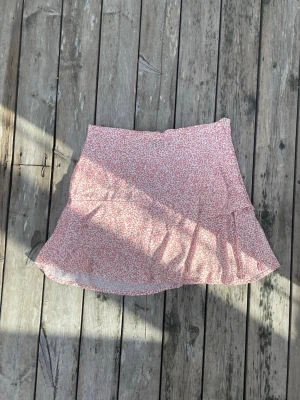 Somrig rosa kjol - Söt kjol i tunt och blommigt tyg. Enkel dragkedja på sidan och med volang. 