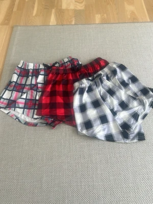 3-pack rutiga pyjamasshorts - Säljer ett 3-pack pyjamasshorts från shein i olika rutiga mönster. Ett par är röd-svarta, ett par är blå-vit-röda och ett par är blå-vita. Alla har resår i midjan och är gjorda i mjukt, tunt tyg som känns skönt mot huden. Perfekta för chill dagar hemma eller mysiga nätter. De är i storlek 150.