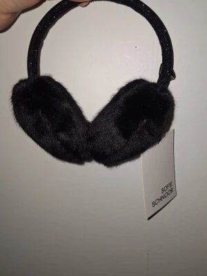 Svarta öronmuffar Sofie Schnoor - Mysiga svarta öronmuffar från Sofie Schnoor med fluffig fuskpäls och böjbar båge. Perfekta för kalla dagar när du vill hålla öronen varma och samtidigt se stilren ut. Köpte dem till en tjej som är 10 år, men upptäckte tyvärr att de är för små, så därför säljer jag dem vidare.