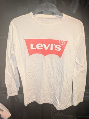 Vit långärmad Levi's tröja - Snygg vit långärmad tröja från Levi's med det klassiska röda logotrycket på bröstet. Tillverkad i mjuk bomull och har en avslappnad passform. Inga synliga fläckar eller defekter. Skapa en bundle för bättre pris