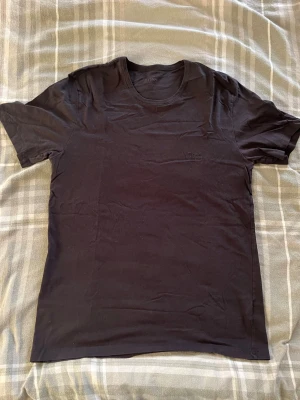 Svart t-shirt från Hugo Boss - Snygg svart t-shirt från Hugo Boss med diskret broderad logga på bröstet. Klassisk rund halsringning och korta ärmar. Tillverkad i mjuk bomull som känns skön mot huden. Perfekt basplagg för en clean och stilren look.