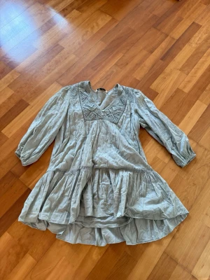 Ljusgrön volangklänning från Zara - Supersöt ljusgrön klänning från Zara med broderade detaljer vid halsen, v-ringning och volang nedtill. Klänningen har trekvartsärm och är tillverkad i ett mjukt bomullstyg. Perfekt för dig som gillar en avslappnad men ändå stylish look.