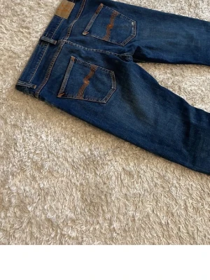 Mörkblå Nudie jeans - Modell: grim tim indigo myth. Säljer ett par mörkblå jeans med raka ben och snygga kontrastsömmar på bakfickorna. Klassisk femficksmodell i denim med normal midja. Perfekta till en avslappnad streetwear-look.
