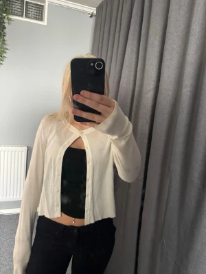 Vit cropped kofta med knappar - Stilren vit cropped kofta med rund hals och knäppning framtill. Långa ärmar och mjukt, tunt material som ger en avslappnad look. Perfekt att slänga över ett linne eller topp för en enkel och trendig outfit.