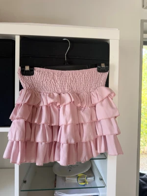 Ljusrosa volangkjol  - Supersöt ljusrosa kjol med flera lager volanger och bred smockresår i midjan och under finns inbyggda shorts. Endast testas, har bara legat i garderoben.