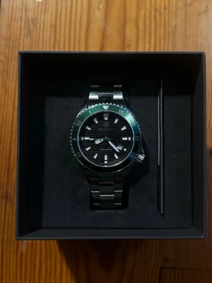 GANT Waterville KM Edition - GANT Waterville KM Edition 45mm – G174003-KM  Säljer min GANT Waterville KM Edition 45mm. En stilren och rejäl klocka med svart urtavla, silverfärgat stålarmband och grön bezel.  Klockan är använd och har tydliga tecken på slitage, bland annat mindre repor/märken på boett och armband. 