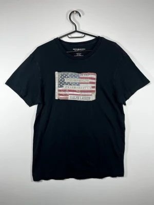 Svart Denim & Supply Ralph Lauren T-shirt med stor USA-flagga i tyg/applikation framtil - Riktigt snygg vintage-inspirerad design med distressed detaljer och broderade sömmar. En modell som sticker ut betydligt mer än vanliga Ralph Lauren T-shirts.  • Storlek M • 100% bomull • Svart • USA-flagga/applikation framtill • Denim & Supply Ralph Lauren • Fint begagnat skick  📏 Mått kan skickas vid önskemål 📦 Skickas snabbt och välpaketerat  