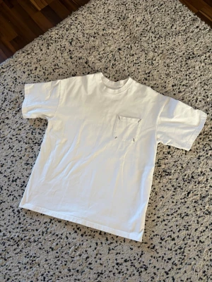 Vit t-shirt med bröstficka Maison Margiela - Vit t-shirt från Maison Margiela med klassisk passform och en liten bröstficka. T-shirten har rund halsringning och är tillverkad i mjuk bomull. Perfekt basic-plagg för en clean och stilren look.