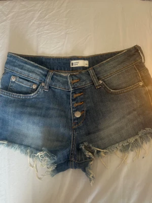 Lågmidjade blå jeansshorts med fransig kant - Säljer ett par blå jeansshorts med låg midja och fransig kant. Väldigt populära och snygga men säljer då dessa också blivit för små. Är i bra skick från ginatricot.