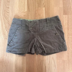Militär gröna manchester shorts med knappar - Snygga gröna shorts i manchester med hög midja och bred linning. Shortsen har fram- och bakfickor med knappdetaljer samt uppvikta benslut. Perfekta för en avslappnad och trendig stil.