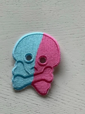 Bubs Patch dödskalle rosa och blå bubbelgum - Broderat tygmärke i form av en dödskalle med korslagda ben, delad i ljusblått och rosa. Märket är ca 7 cm högt och har två hål för ögon. Perfekt att sy eller stryka på jacka, väska eller keps för en unik look.