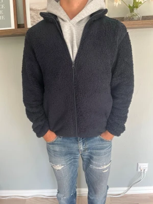 Uniqlo Fleecejacka Svart XS Fusion - Uniqlo fleecejacka i svart, mjukt luddig fleece-textur med genomgående blixtlås och krage. Avslappnad passform, funkar som mellanlager eller lätt ytterplagg.  Skick: bra skick, inga hål eller fläckar Material: fleece (polyester) Storlek: XS Modell: 175 cm / 65 kg — sitter true to size på bild  