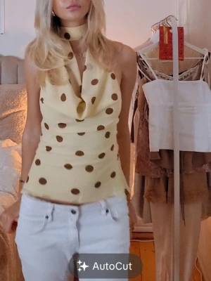 Gul prickig halterneck topp - Trendig gul halterneck topp med bruna prickar och en snygg scarfdetalj runt halsen. Perfekt för sommarens alla tillfällen. Tillverkad i ett mjukt och lätt material som ger en skön känsla.