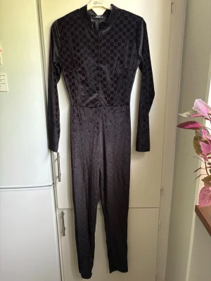Snygg byxdress med mönster på. - Svart byxdress med mönster på. Dragkedja baktill. Bälte till. Står storlek S, men tycker att den passar en XS bättre. Man ser mönster bäst på sista bilden. Aldrig använd, bara legat i garderoben.