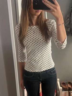 Vit prickig topp med trekvartsärm - Snygg vit topp med svarta prickar och trekvartsärm. Modellen är figurnära och har en klassisk rund halsringning. Perfekt att styla med jeans eller kjol för en trendig look. Endast testad💕💕