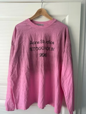 Acne studio sleeve rosa - Säljer en rosa långärmad t-shirt från Acne Studios med tryck 'STOCKHOLM 1996' på bröstet. Tröjan har en klassisk rund hals och är gjord i mjuk bomull. Perfekt för dig som gillar streetwear och vill ha något som sticker ut.