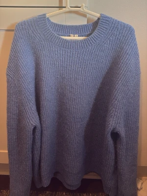 Stickad tröja från Arket - Mysig blå stickad tröja med rund halsringning och avslappnad, oversized passform. Tröjan har långa ärmar och ribbstickade muddar vid hals, ärmslut och nederkant. Perfekt för lager på lager och chill dagar.