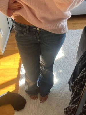 Mörkblå bootcut jeans, storlek 34 - Säljer ett par mörkblå bootcut jeans med klassisk femficksmodell och vita kontrastsömmar. Jeansen har låg midja och är i stretchigt denimtyg för skön passform. 