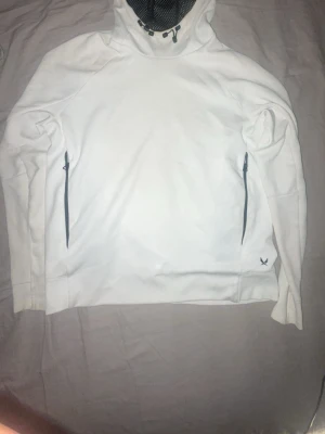 Vit hoodie från SOC med dragkedjor - Säljer en vit hoodie från SOC i storlek S. Hoodien har huva med justerbar dragsko och meshfoder, samt två svarta dragkedjefickor framtill. Tillverkad i ett mjukt material som passar perfekt för chill eller träning.