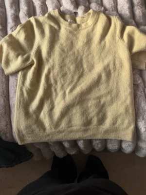 Gul stickad kortärmad tröja - Mysig gul stickad tröja med korta ärmar och rund halsringning. Tröjan har ribbade muddar vid ärmslut och nederkant, vilket ger en avslappnad men ändå stilren look. Perfekt för lager på lager och vårens outfits.