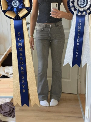 Grå bootcut jeans med medelhög midja - Säljer ett par gråa bootcut jeans med medelhög midja och klassiska fem fickor. Jeansen har en snygg tvätt och raka ben som går ut lite nedtill. Perfekta till en enkel topp eller hoodie för en chill look.