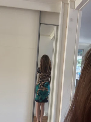 Kort leopardmönstrad klänning - Snygg kort klänning med leopardmönster i brunt och svart samt stora turkosa blommor nertill. Klänningen har korta svarta ärmar och rak passform. Perfekt för dig som vill sticka ut med ett djärvt mönster och färgkombination. Passar s och även xs