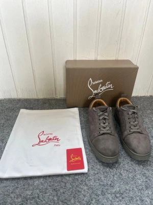 Gråa Christian Louboutin sneakers - Snygga gråa sneakers från Christian Louboutin i mocka med röda sulor, pris kan diskuteras och om man vill ha fler bilder är det bara att fråga!