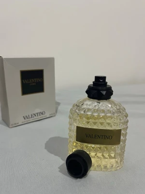 Valentino Uomo Eau de Toilette 100ml - Lyxig parfym från Valentino i en elegant, genomskinlig glasflaska med nitar och gul etikett. Flaskan har en svart spraykork och kommer med originalkartong. Doften är klassisk och tidlös, perfekt för dig som vill ha något exklusivt i badrumsskåpet.