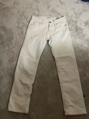 Vita raka jeans - Säljer ett par vita jeans med rak passform och klassisk femficksdesign. Jeansen har normal midja och stängs med knapp och dragkedja. Materialet är kraftigt denim som ger en snygg och stilren look.