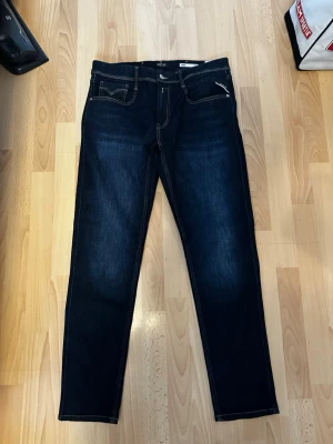 Mörkblå Replay Anbass - Nya replay anbass jeans i storlek 33/32. Ordinarie pris 1899. Snygga mörkblå slim fit jeans från Replay med klassisk femficksmodell och kontrastsömmar. Jeansen har raka ben och är tillverkade i ett stretchigt denimtyg för extra komfort. Bakfickorna har dekorativa sömmar och Replay-logga.