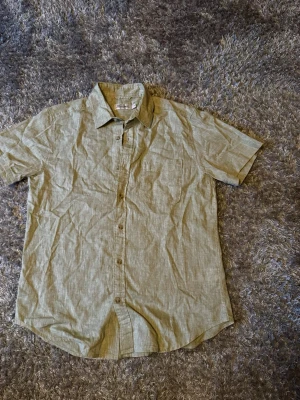 Ljusgrön linneskjorta från Dressmann - Snygg ljusgrön skjorta från Dressmann i linnemix. Skjortan har korta ärmar, klassisk krage, bröstficka och knappar framtill. Perfekt för varma dagar och enkel att styla till olika outfits.