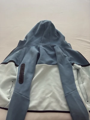Nike blå och vit hoodie XL - Snygg hoodie från Nike i blått och vitt med dragkedjeförsedd ficka på ärmen och svarta detaljer. Tillverkad i mjukt material och har en stor huva. Perfekt för en chill och sportig look. Köpte den för 2 veckor sen jag har inte använd den den är helt ny pris kan diskuteras.